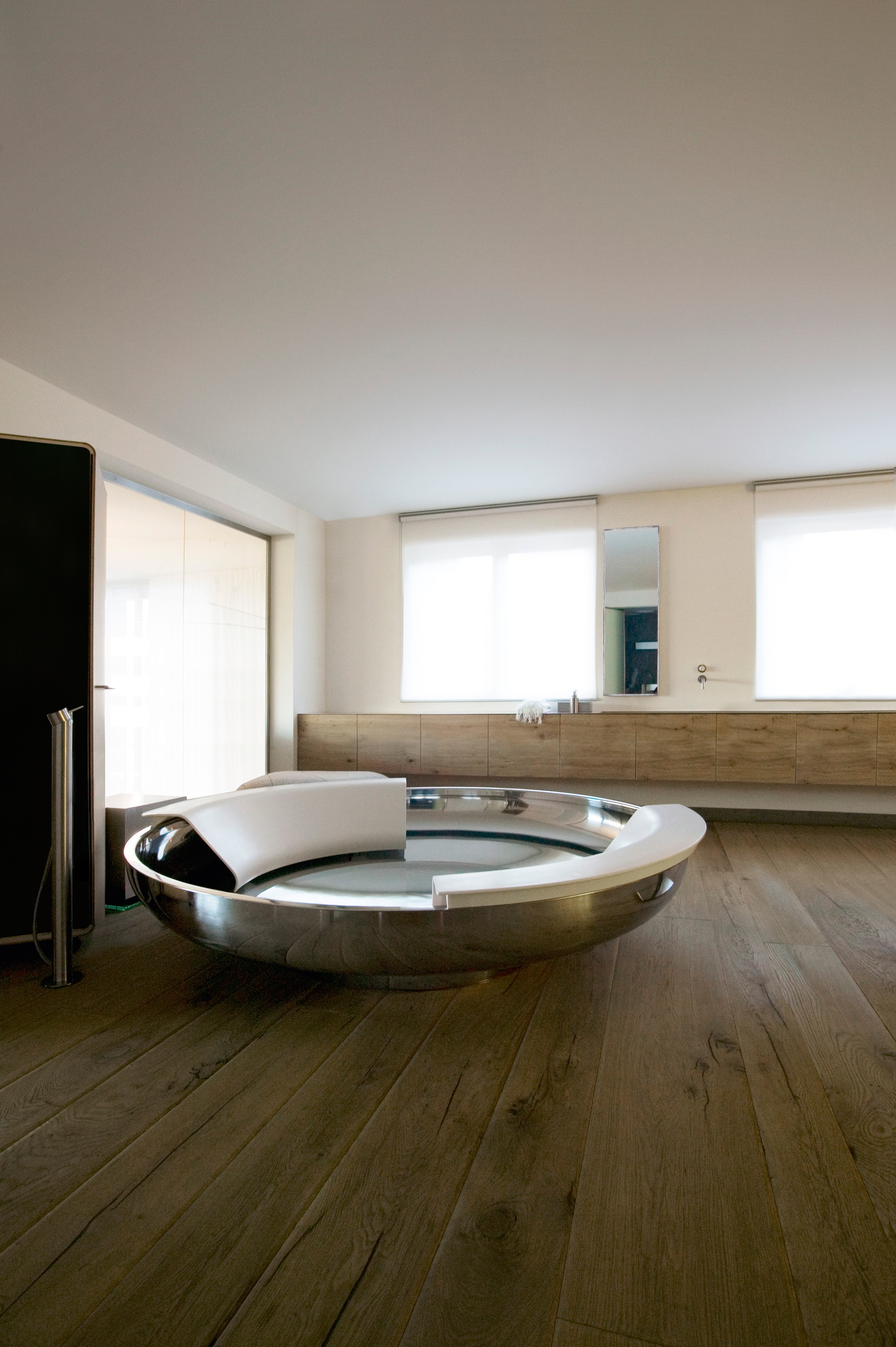Freistehende runde Badewanne Ufo von Agape aus glänzendem Edelstahl mit weißer Cristalplant Rückstütze, Design Benedini Associati, in einem luxuriösen Badezimmer mit Holzfußboden.
