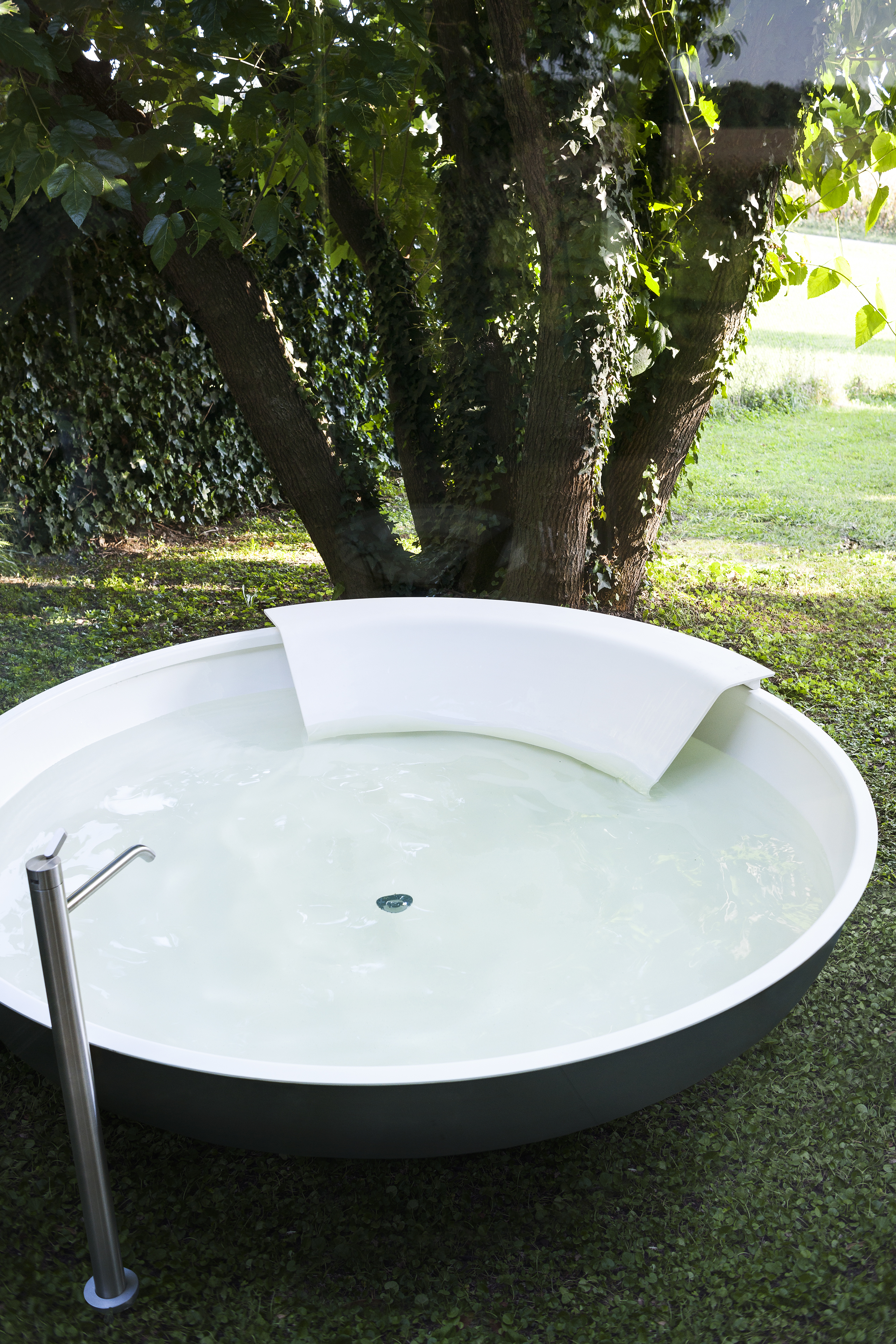 Outdoor Badewanne Ufo von Agape mit dunkelgrau lackierter Außenseite und weißer Cristalplant® Rückstütze, Design Benedini Associati, auf einer Rasenfläche unter einem Baum.